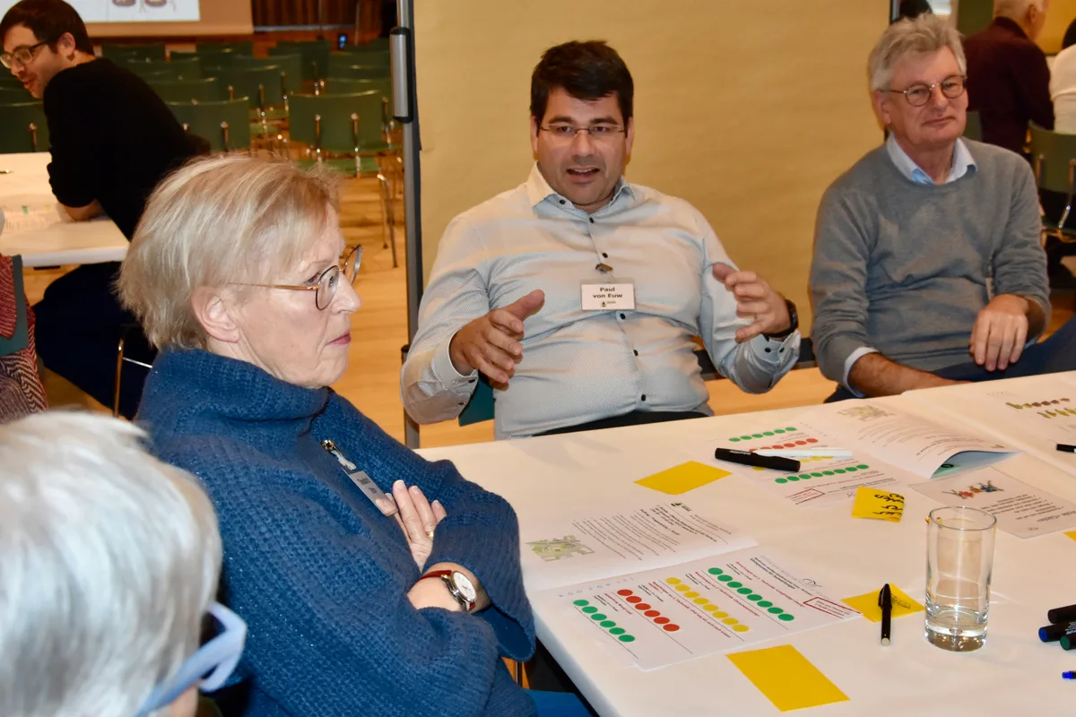 Ein Mann spricht und gestikuliert. Die anderen rundherum hören zu.
